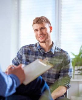 Smiling young student talking to therapist. Man is discussing with mental health professional. They are sitting in lecture hall at university.